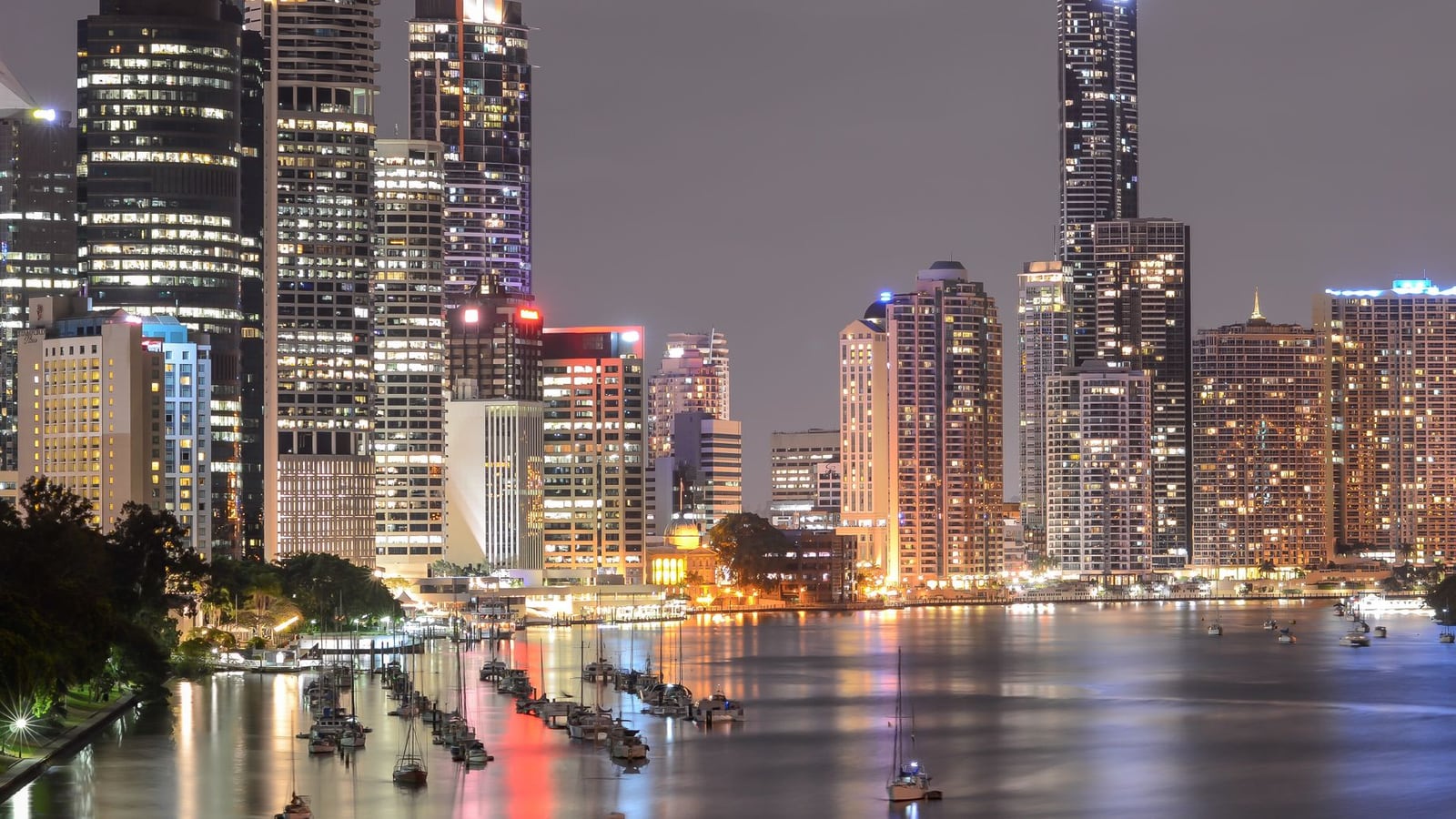 A wide cinematic view of the Brisbane city skyline under a clear blue sky.